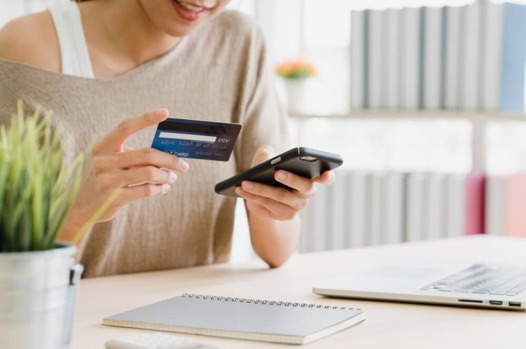 Mulher com cartão de crédito fazendo compras pelo celular.