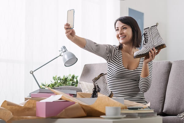 Mulher tira selfie com coturno para mostrar embalagens de calçado