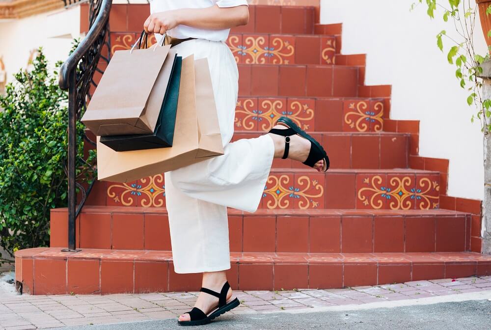 Mulher usando sandálias pretas e segurando sacolas de compras.